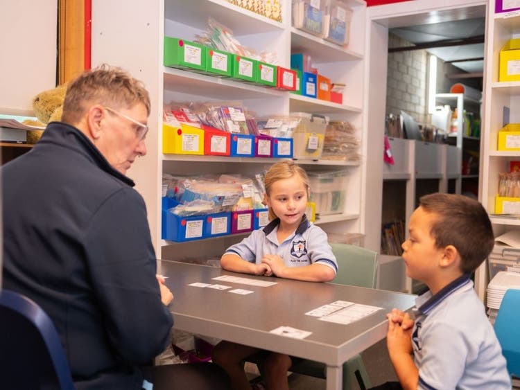 photo of a support teacher helping a girl and boy with individual help sitting at a table together