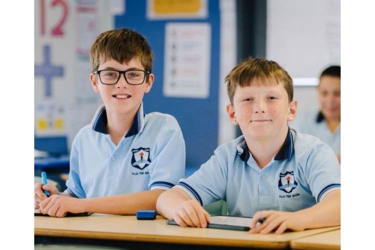 ttwo boys sitting at a desk looking up from their work
