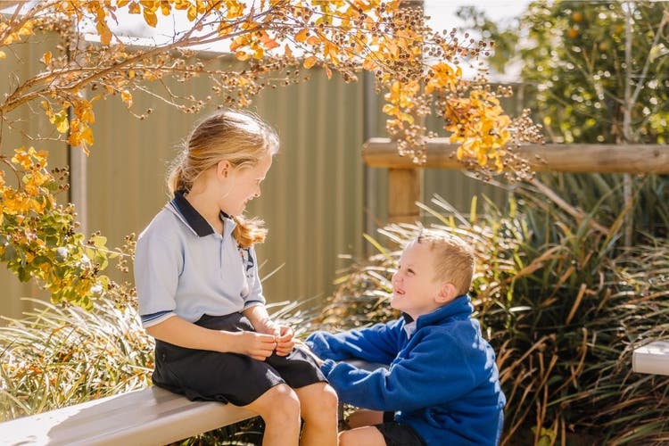Girl sitting out side looking down at a boy squatting next to her surrounded by bushes